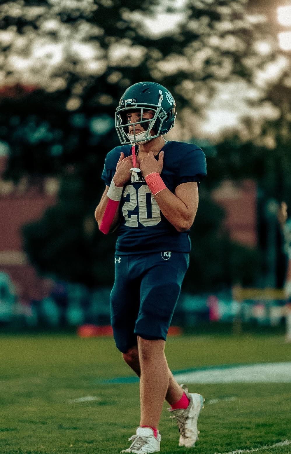 Walker Andrews in a navy Nobles football uniform, number 20, walking on the field in helmet and pads.