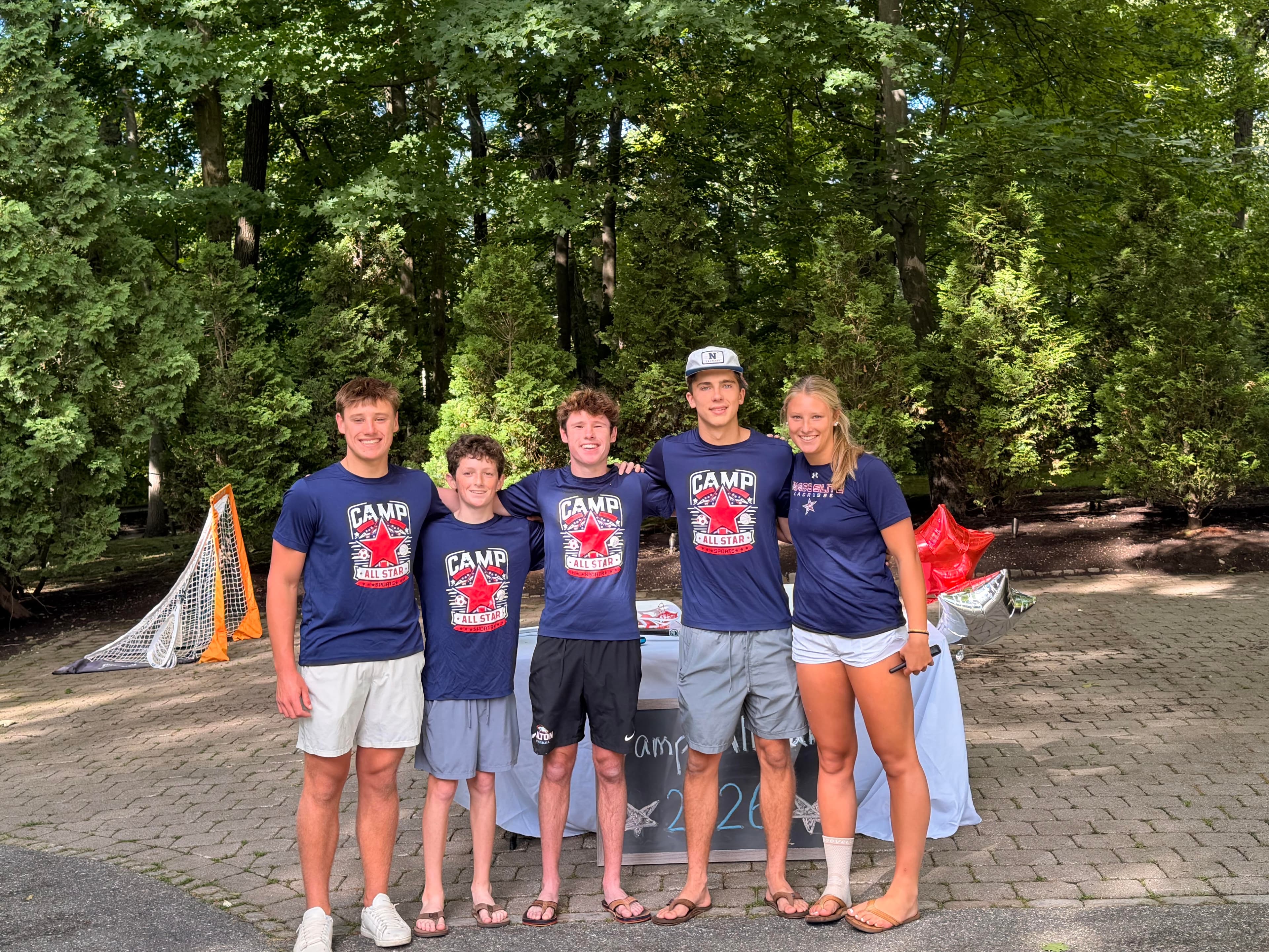The five Camp AllStar coaches standing together in navy Camp AllStar t-shirts in front of a lacrosse goal, 2026 season.