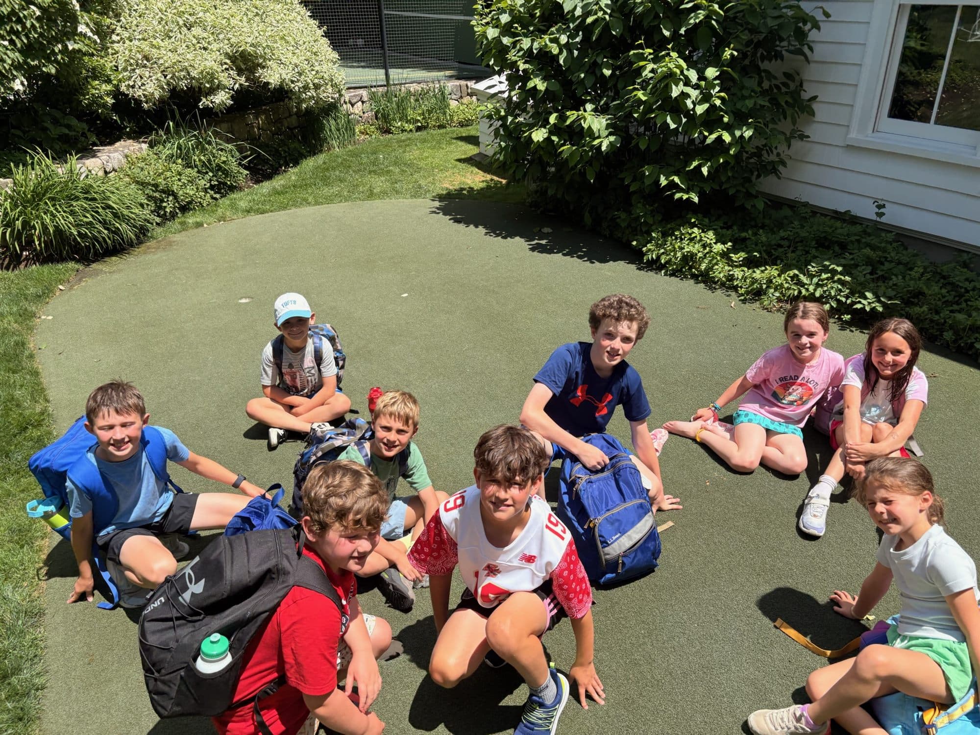 Campers sitting together on the putting green with their backpacks and water bottles.