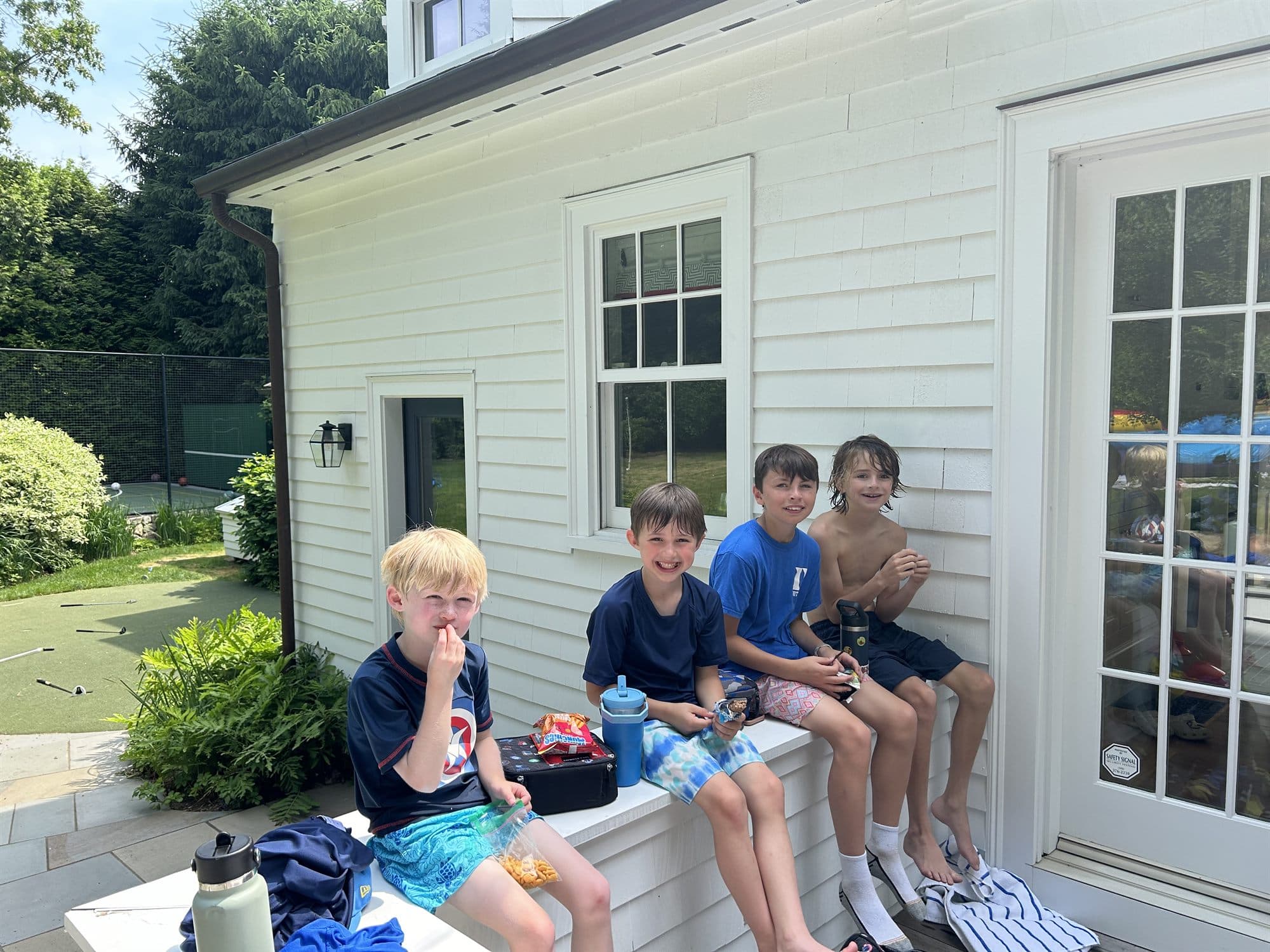 Four campers sitting on a bench in the shade with snacks and drinks during a break.